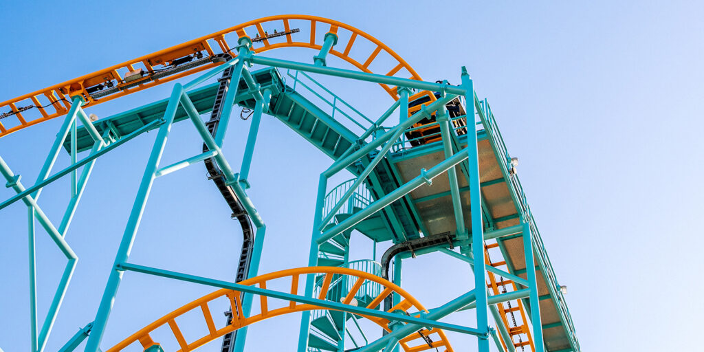 view of twisting orange and teal roller coaster tracks from down below looking up, innovative portfolios perspectives