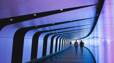 the backs of two people walking down a curved hallway that is illuminated with purple light, innovative portfolios perspectives