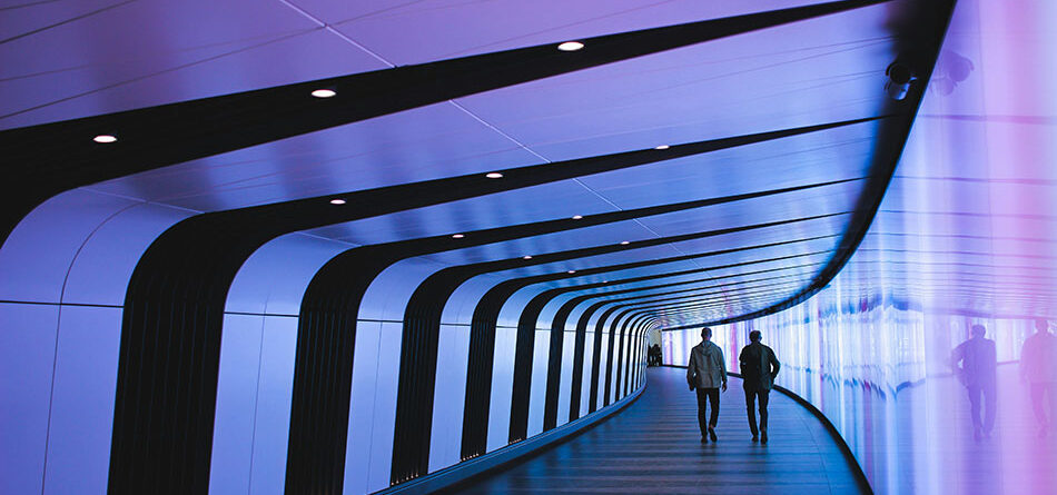 the backs of two people walking down a curved hallway that is illuminated with purple light, innovative portfolios perspectives