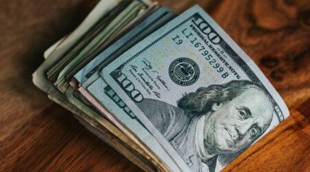 close-up of a folded stack of 100 dollar bills sitting on a wooden tabletop, innovative portfolios perspectives