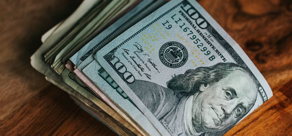 close-up of a folded stack of 100 dollar bills sitting on a wooden tabletop, innovative portfolios perspectives