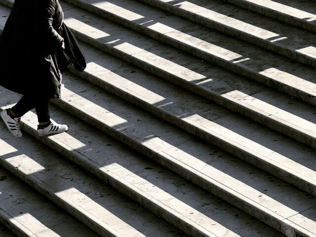 figure dressed in black climbing up marble stairs with light and shadows on the stairs, innovative portfolios perspectives